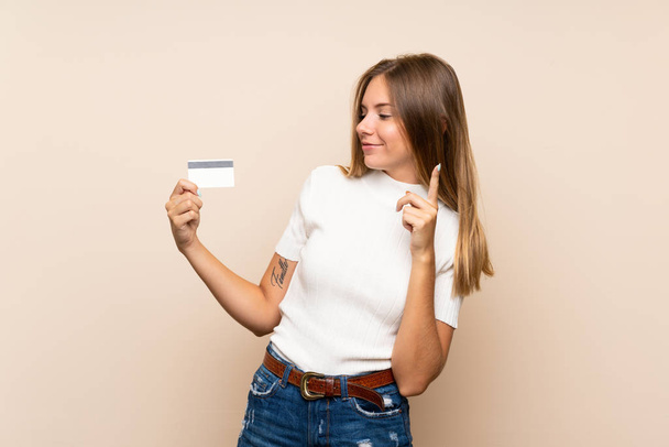 jong blond vrouw over geïsoleerde achtergrond met een credit card - Foto, afbeelding