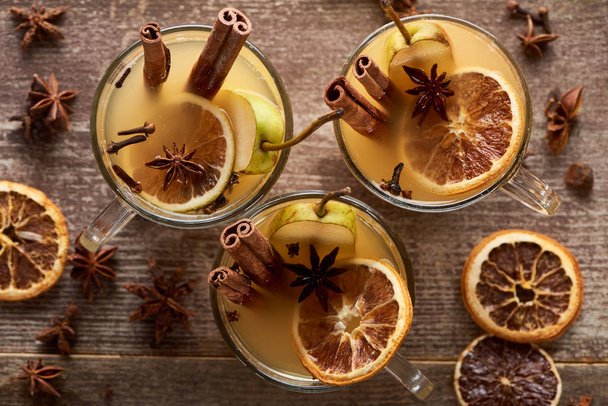 top view of seasonal pear mulled wine cocktails with spices and dried citrus on wooden rustic table - Fotó, kép