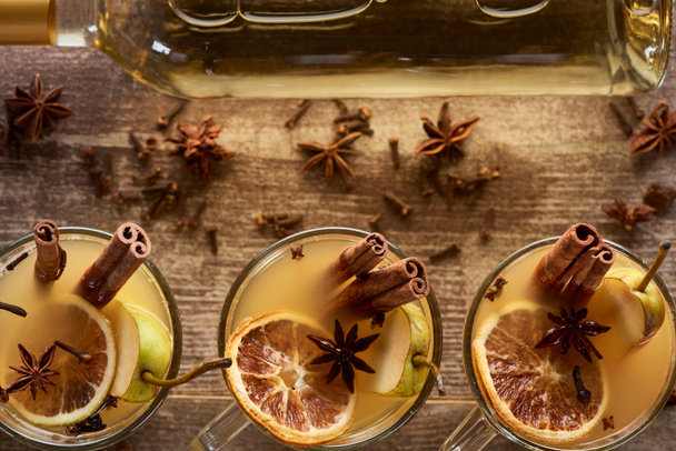 top view of seasonal pear mulled wine cocktails with spices and dried citrus on wooden rustic table - Fotó, kép