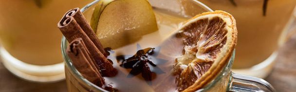 close-up uitzicht op peer glühwein met specerijen en gedroogde citrus op houten tafel, panoramisch schot - Foto, afbeelding