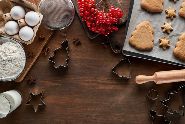 vrchní pohled na vánoční cukroví v blízkosti ingrediencí, těsta formy a viburnum na dřevěném stole - Fotografie, Obrázek
