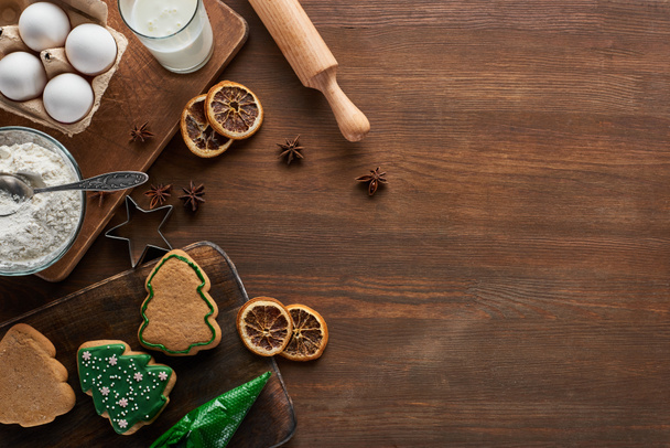 top view νόστιμα χριστουγεννιάτικα μπισκότα κοντά σε συστατικά και μπαχαρικά σε ξύλινο τραπέζι - Φωτογραφία, εικόνα