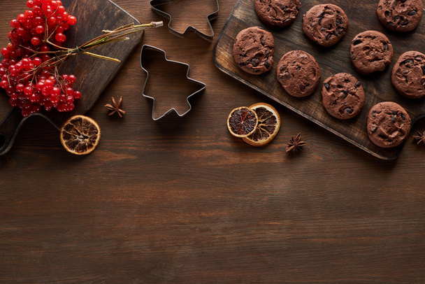 Ansicht von Schokoladenkeksen in der Nähe von Weihnachtsteigformen, Viburnum und Gewürzen auf Holztisch - Foto, Bild