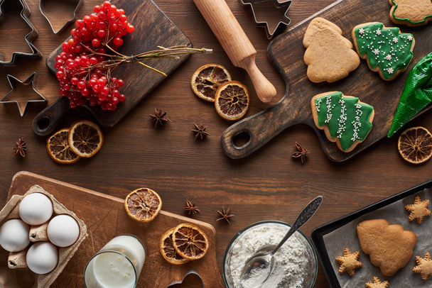 top view of Christmas tree cookies near ingredients and viburnum on wooden table - Foto, Bild