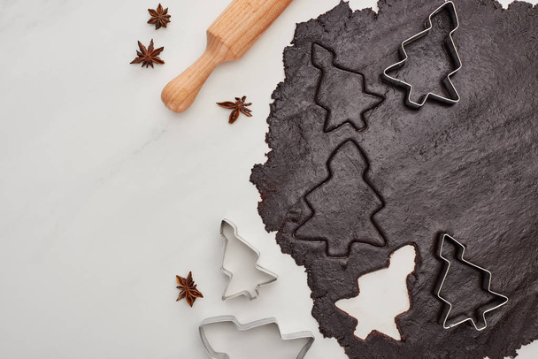 horní pohled na syrové těsto pro čokoládové vánoční cukroví na bílém pozadí v blízkosti anýzu a válečku - Fotografie, Obrázek