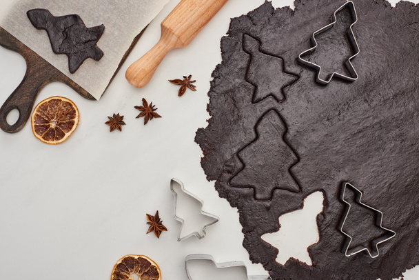 vista superior da massa crua para biscoitos de Natal de chocolate no fundo branco perto de anis, frutas secas e rolo
 - Foto, Imagem