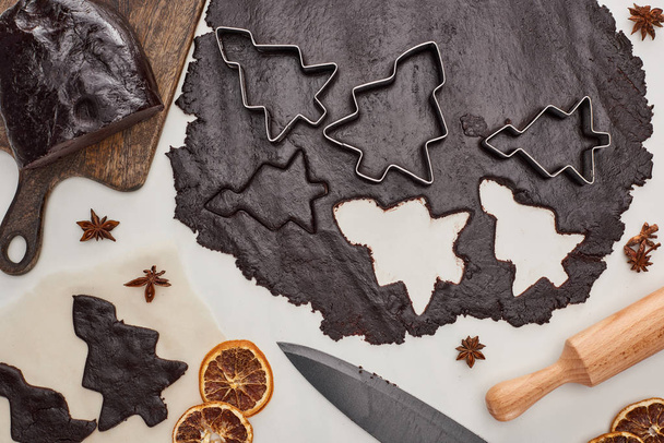vue du dessus de la pâte crue pour biscuits de Noël au chocolat sur fond blanc près de l'anis, couteau et rouleau à pâtisserie
 - Photo, image