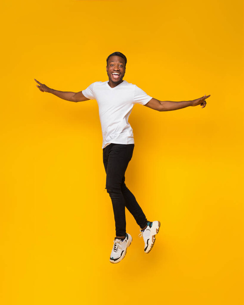 Afrikkalainen amerikkalainen kaveri hyppäämällä ottaa hauskaa yli keltainen tausta
 - Valokuva, kuva