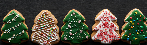 flat lay with delicious glazed Christmas tree cookies on black wooden table, panoramic shot - Фото, зображення