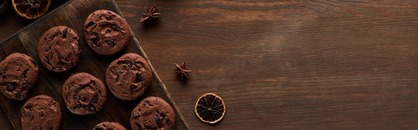 horní pohled na čokoládové sušenky a koření na dřevěném stole s kopírovacím prostorem, panoramatický záběr - Fotografie, Obrázek