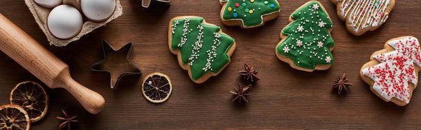 Top view karácsonyfa cookie-k, tészta formák, tojás és sodrófa csap a fa asztalon, panoráma lövés - Fotó, kép