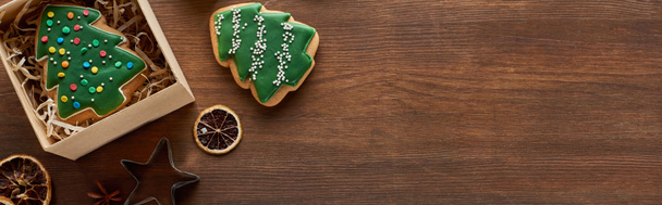top view of Christmas tree cookies, gift box and dried citrus slices on wooden table, panoramic shot, panoramic shot - Fotó, kép