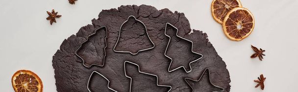 vista superior da massa crua para biscoitos de Natal de chocolate no fundo branco perto de moldes de massa e especiarias de inverno, tiro panorâmico
 - Foto, Imagem