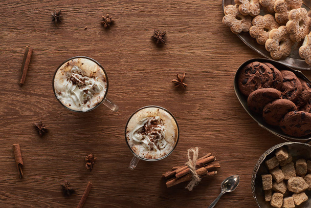 vrchní pohled na vánoční kakao se šlehačkou na dřevěném stole s kořením a sušenkami - Fotografie, Obrázek