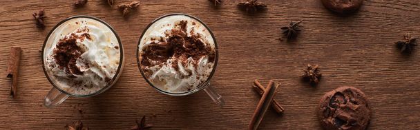 Kurabiye ve baharatların yanında, ahşap masanın üzerinde krem şantili Noel kakaosunun en üst görüntüsü. - Fotoğraf, Görsel