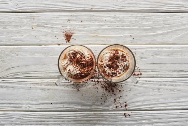 вид сверху на какао со взбитыми сливками и порошком какао в кружках на белом деревянном столе
 - Фото, изображение