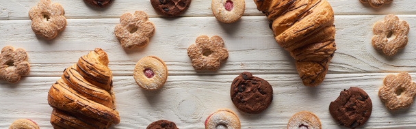 Draufsicht auf süße Kekse und Croissants auf weißem Holztisch, Panoramaaufnahme - Foto, Bild