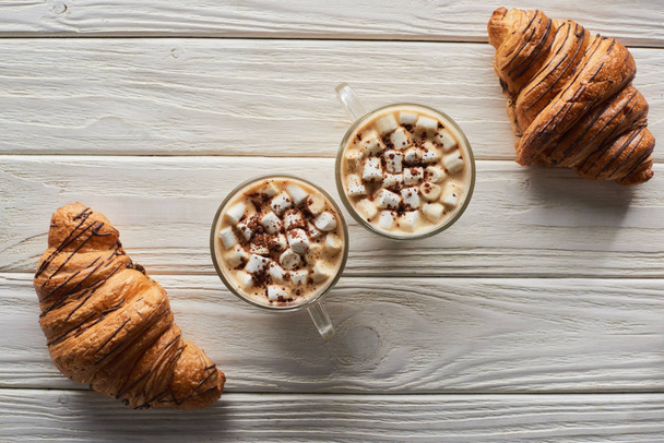 vrchní pohled na kakao s marshmallow u sušenek a croissanty na bílém dřevěném stole - Fotografie, Obrázek