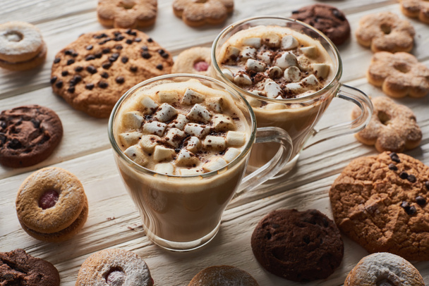 Kakao mit Marshmallow in Tassen neben Keksen auf weißem Holztisch - Foto, Bild