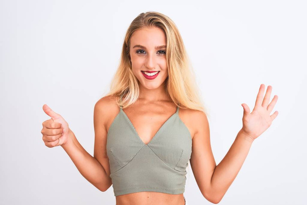 Young beautiful woman wearing casual green t-shirt standing over isolated white background showing and pointing up with fingers number six while smiling confident and happy. - Photo, Image