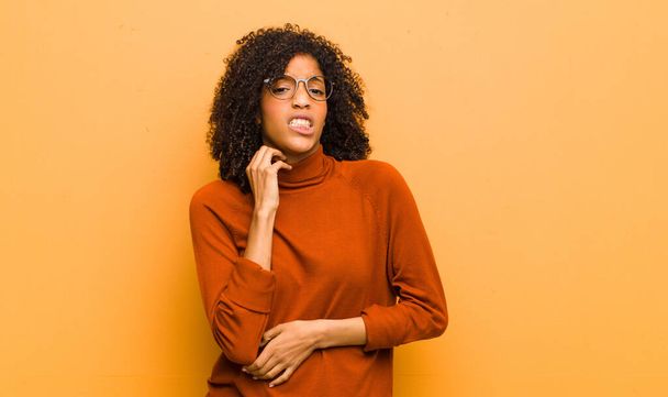 young pretty black woman feeling stressed, frustrated and tired, rubbing painful neck, with a worried, troubled look against orange wall - Foto, Imagen