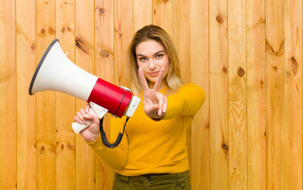 young pretty blonde woman with a megaphone against wood wall - Фото, зображення