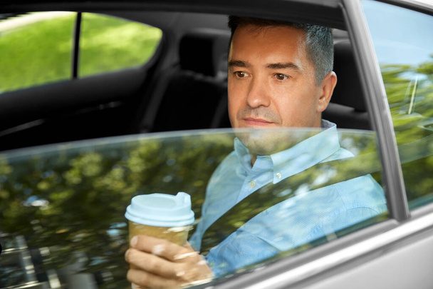 man drinking takeaway coffee on car back seat - 写真・画像