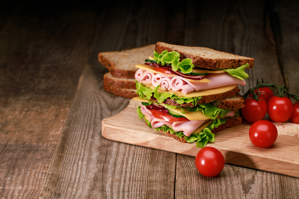 fresh sandwich with lettuce, ham, cheese, bacon and tomato on wooden cutting board with cherry tomato - Valokuva, kuva