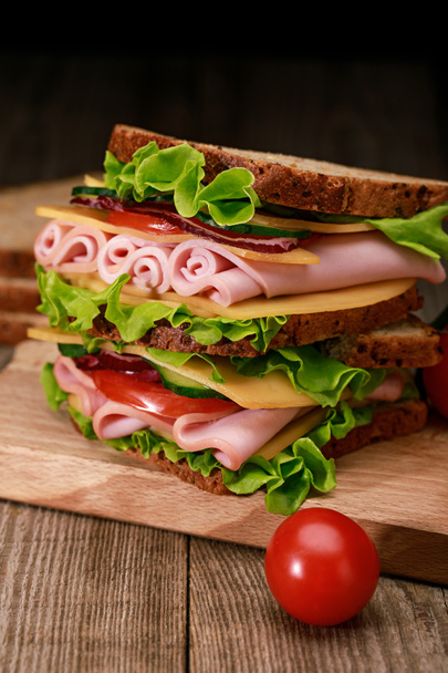 fresh sandwich with lettuce, ham, cheese, bacon and tomato on wooden cutting board with cherry tomato - 写真・画像
