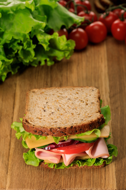 selective focus of fresh sandwich on wooden cutting board near lettuce and cherry tomatoes - Zdjęcie, obraz