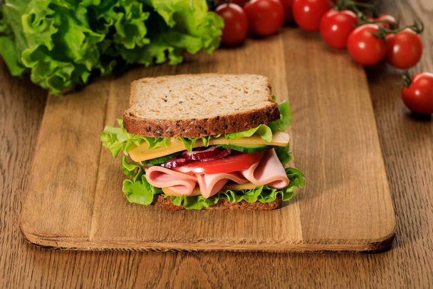 selektiver Fokus von frischem Sandwich auf Holzschneidebrett in der Nähe von Salat und Kirschtomaten - Foto, Bild