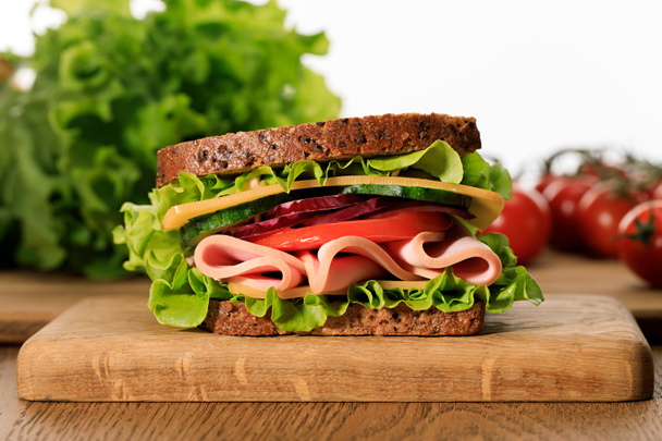 frisches Sandwich mit Salat, Schinken, Käse, Speck und Tomate auf einem Holzschneidebrett isoliert auf weiß - Foto, Bild