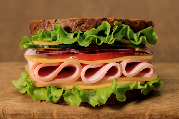 fresh sandwich with lettuce, ham, cheese, bacon and tomato on wooden cutting board - 写真・画像