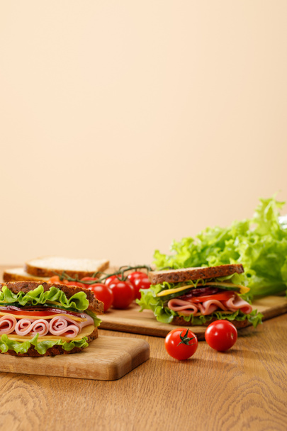 selective focus of fresh sandwich near lettuce, bread, cherry tomatoes on wooden table isolated on beige - 写真・画像