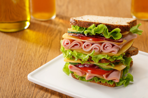 enfoque selectivo de sándwich fresco con lechuga, jamón, queso, tocino y tomate cerca de botellas de cerveza en la mesa de madera
 - Foto, Imagen