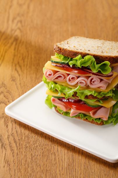 fresh sandwich with lettuce, ham, cheese, bacon and tomato at wooden table - Foto, afbeelding