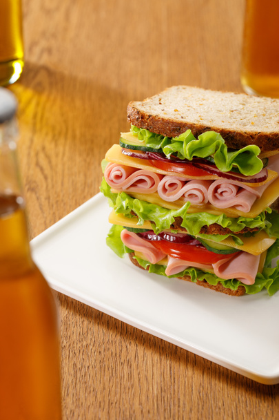 selective focus of fresh sandwich with lettuce, ham, cheese, bacon and tomato near bottles of beer at wooden table - Foto, Imagen