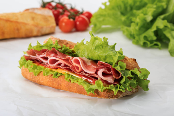 selective focus of fresh sandwich with lettuce, ham, cheese, bacon and tomato on textured white background - Photo, Image