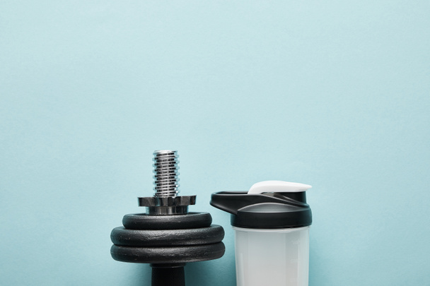 top view of dumbbell near sports bottle with protein shake on blue  - Photo, Image