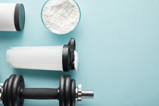 top view of dumbbell near sports bottle and protein powder on blue  - Fotografie, Obrázek