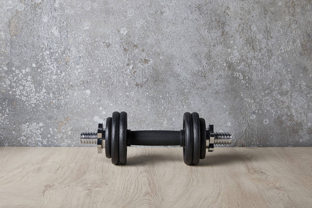 halteres pesados e pretos na superfície de madeira perto da parede de concreto
  - Foto, Imagem
