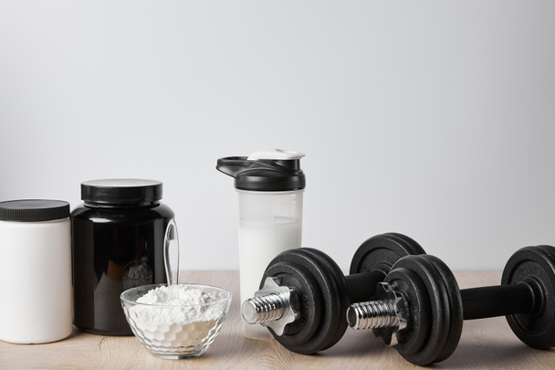 proteinový koktejl ve sportovní láhvi v blízkosti sklenic a činek na bílém  - Fotografie, Obrázek