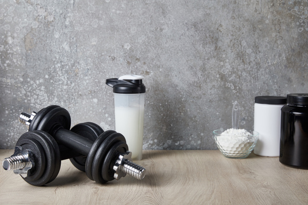 protein shake in sports bottle near dumbbells and protein powder near concrete wall  - Foto, Imagem