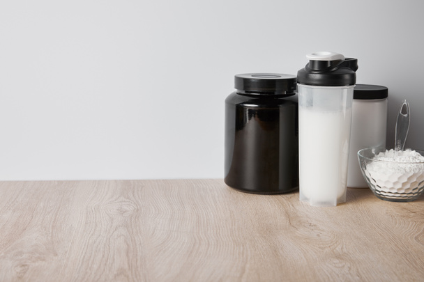 protein shake in sports bottle near jars and glass bowl with protein powder isolated on grey - Photo, Image