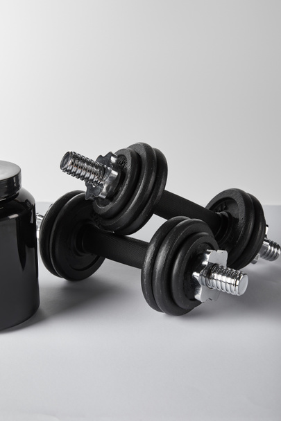 black jar with protein near heavy dumbbells on white  - Foto, afbeelding