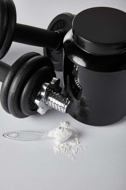 jar near dumbbells and spoon with protein powder on white  - Photo, Image