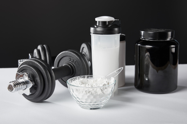 selective focus of bowl near dumbbells and sports bottle with protein shake on black  - Foto, Bild