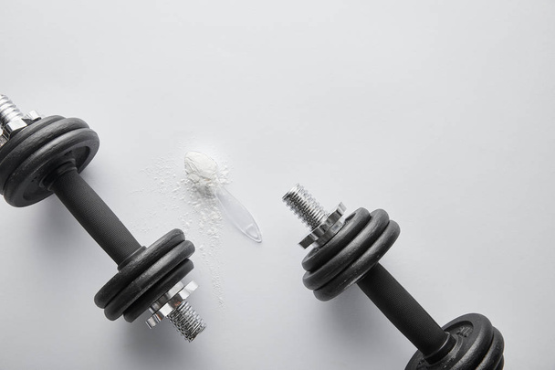 ylhäältä lusikka proteiinijauheella lähellä raskaita käsipainoja valkoisella
  - Valokuva, kuva