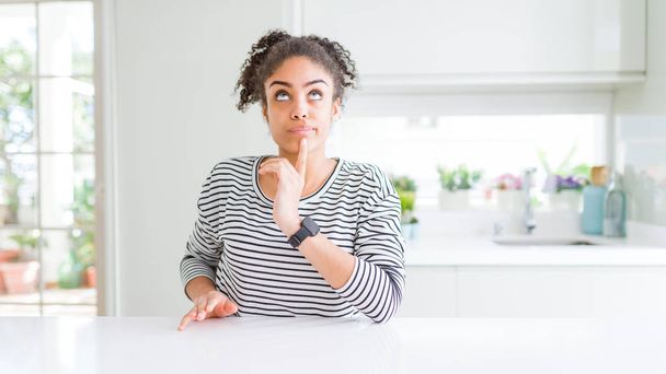 Красивая африканская американка с афроволосами в обычном полосатом свитере думает о сомнении с пальцем на подбородке и смотрит вверх, удивляясь:
 - Фото, изображение