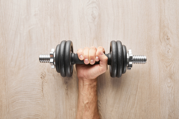 top view of sportsman holding dumbbell near wooden surface  - Photo, image